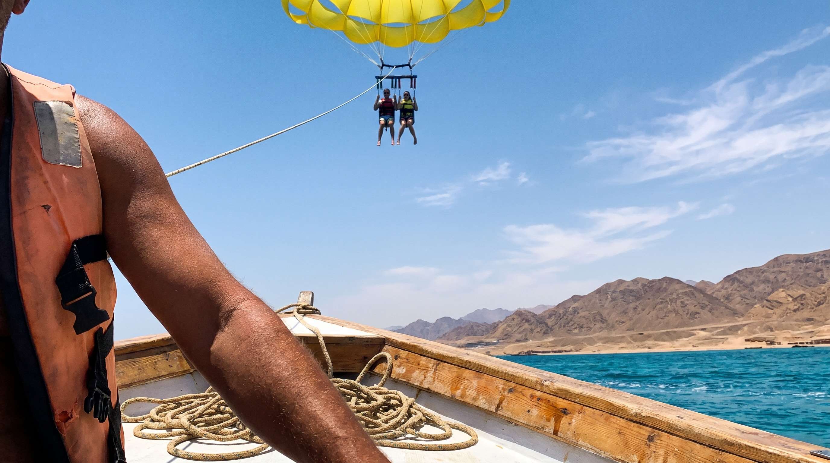 Two guests parasailing under a yellow canopy above the turquoise Red Sea and the Sinai mountains