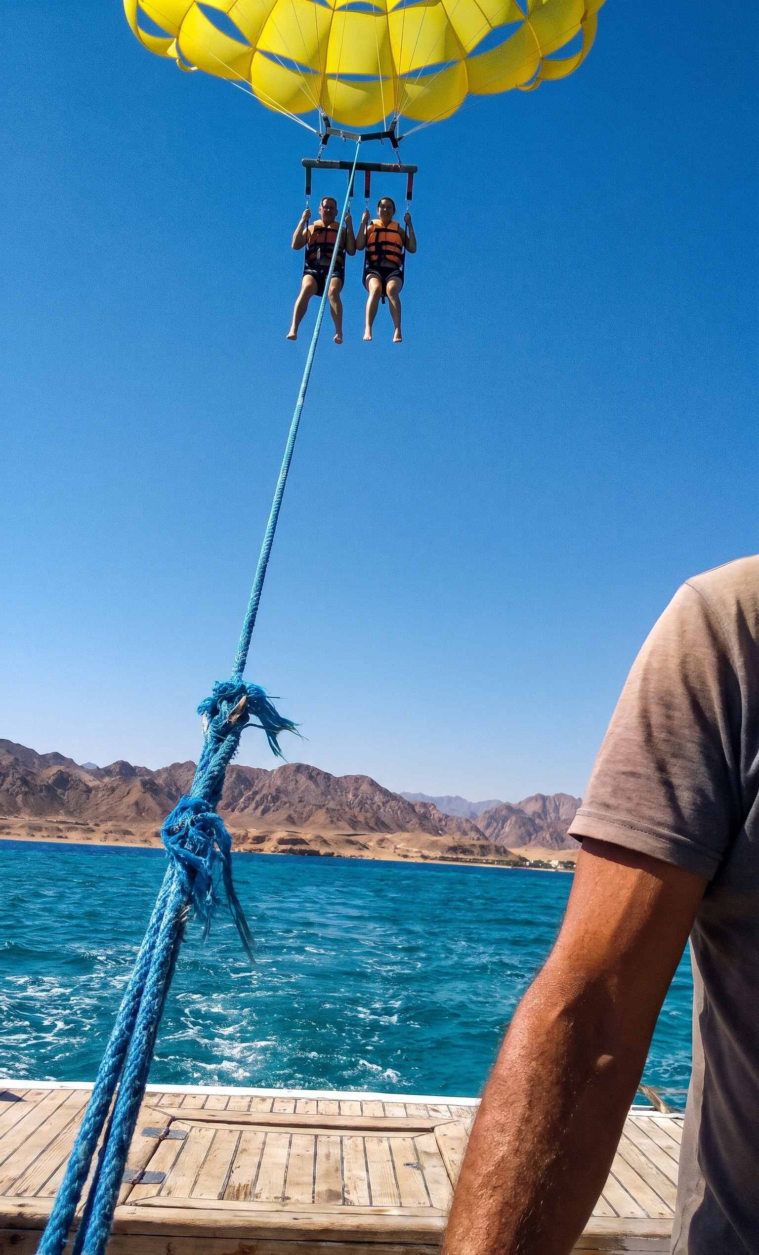 Two guests under a yellow parasail above the Red Sea, seen from the boat