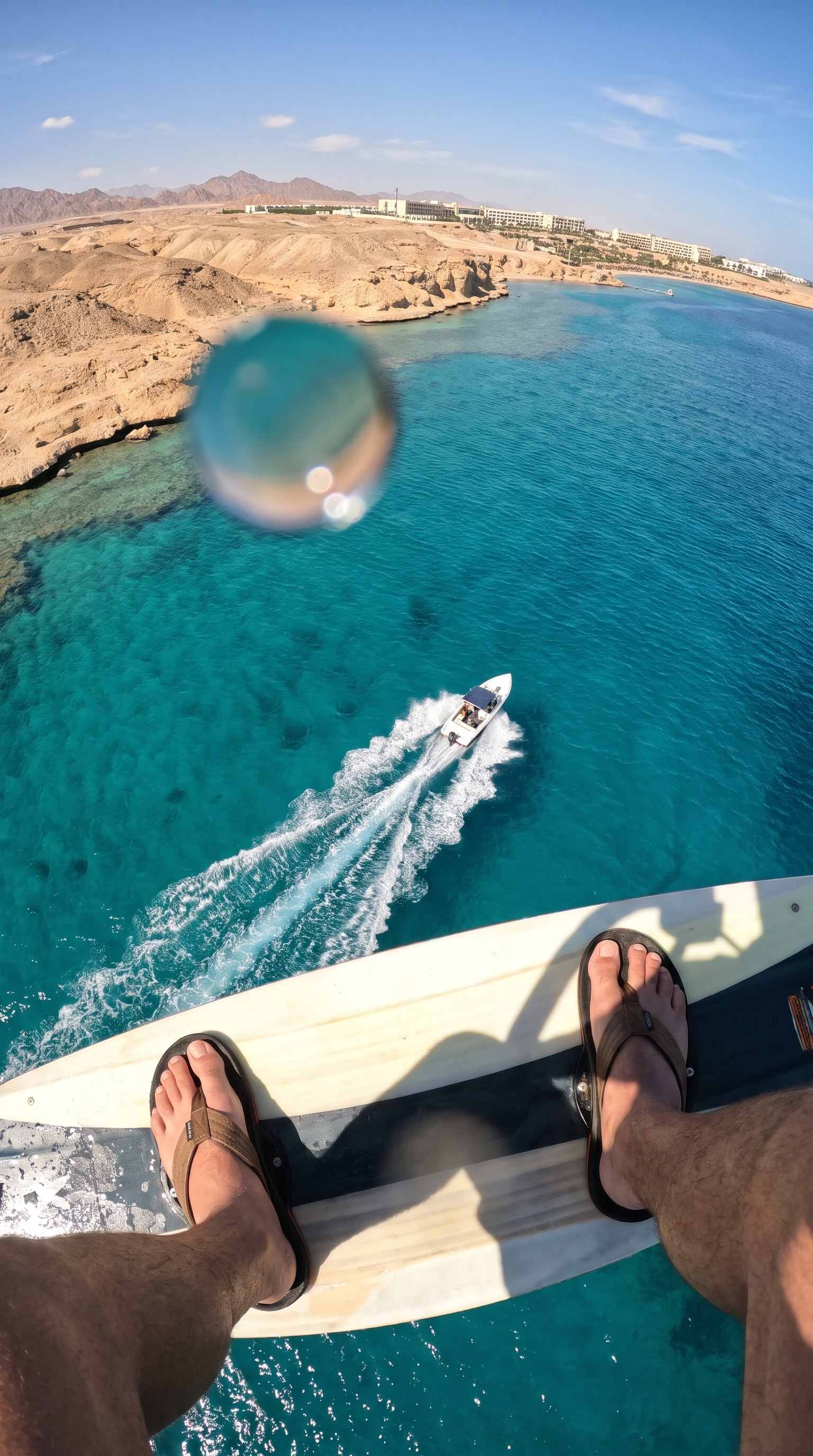 Point-of-view from a parasail over the turquoise reef and the boat below