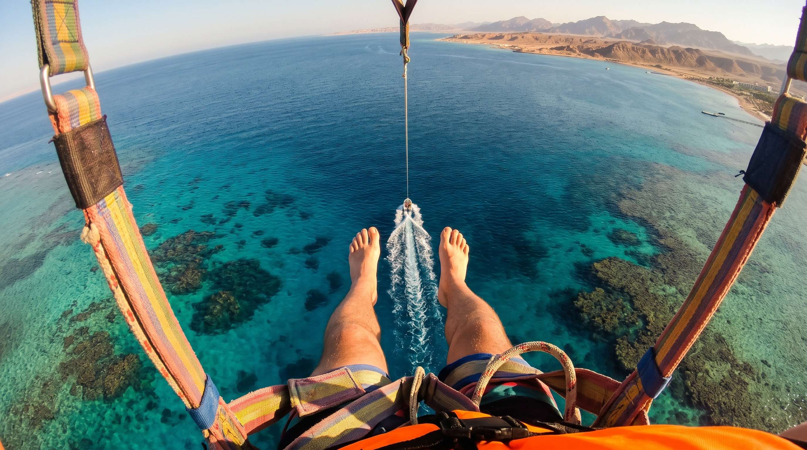 Two guests parasailing under a yellow canopy above the turquoise Red Sea and the Sinai mountains