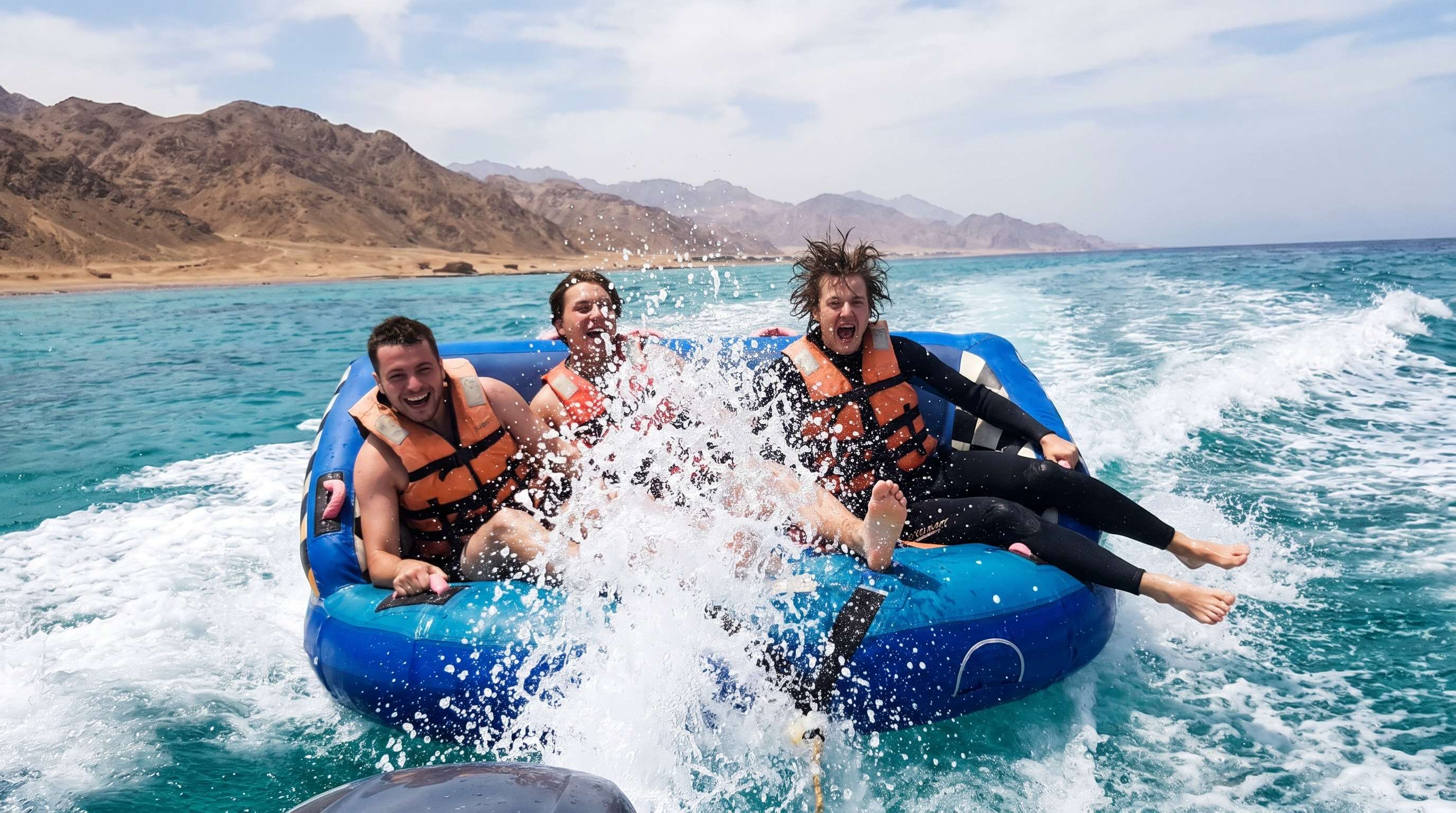 Friends laughing on an inflatable tube ride behind a speedboat