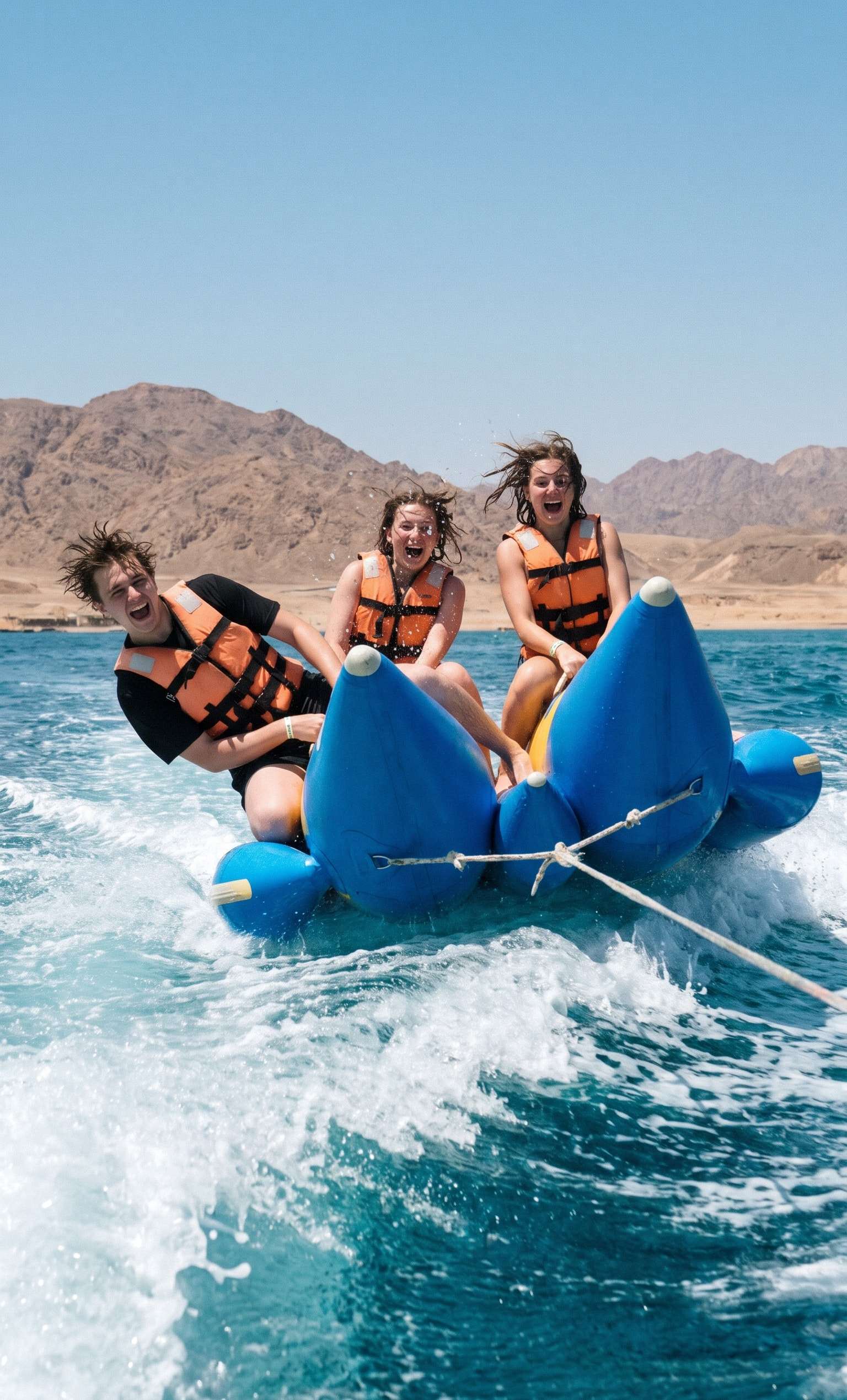 Three friends on an inflatable sofa tube splashing over the waves